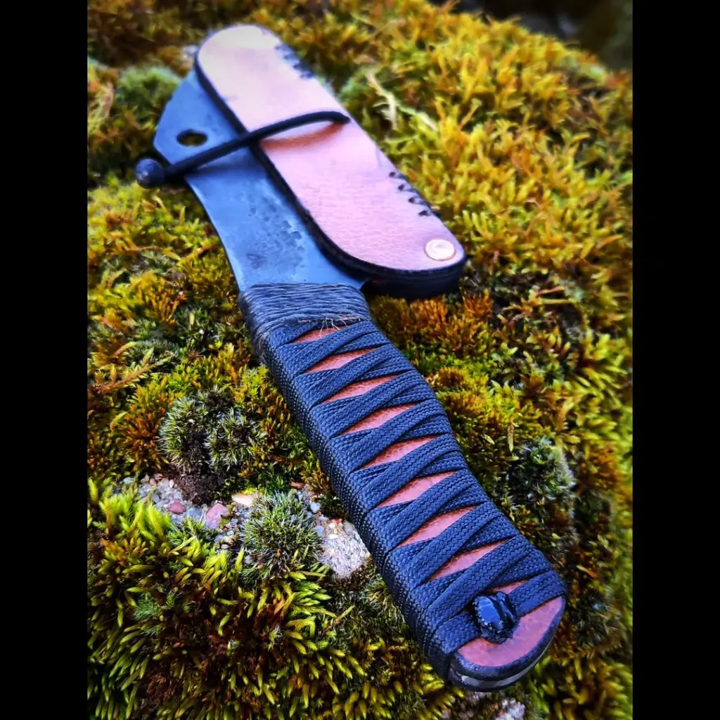 Couperet de camp.Lame en acier xc75, trempe sélective, brut de forge, finition patinée.Manche en cuir, tressage paracorde, ligature chanvre.Protège lame en cuir, rivets laiton, corde élastique, couture chanvre.Dispo....-1.webp